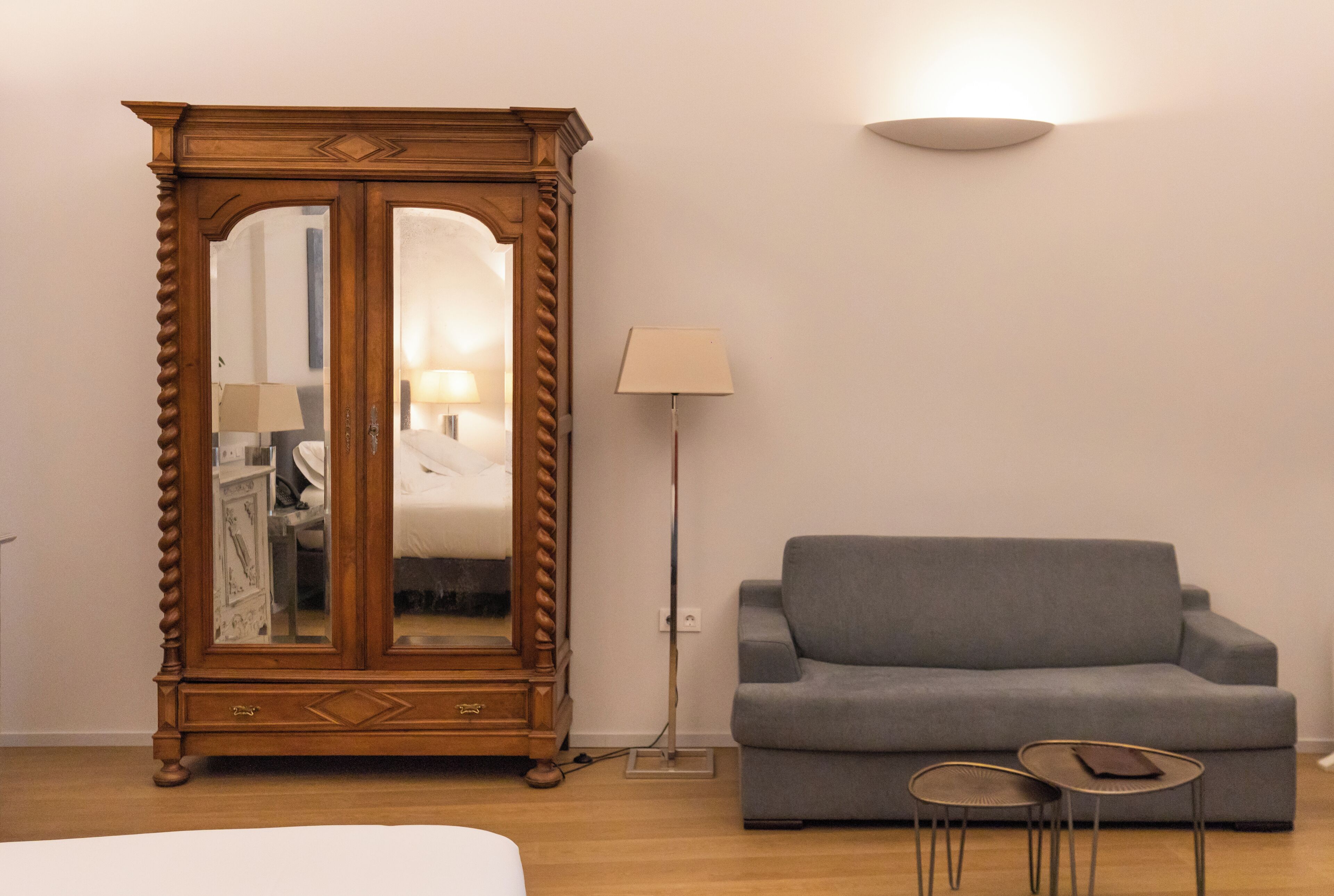 Een kamer met een houten kast, een grijze bank, een vloerlamp en twee kleine tafels.