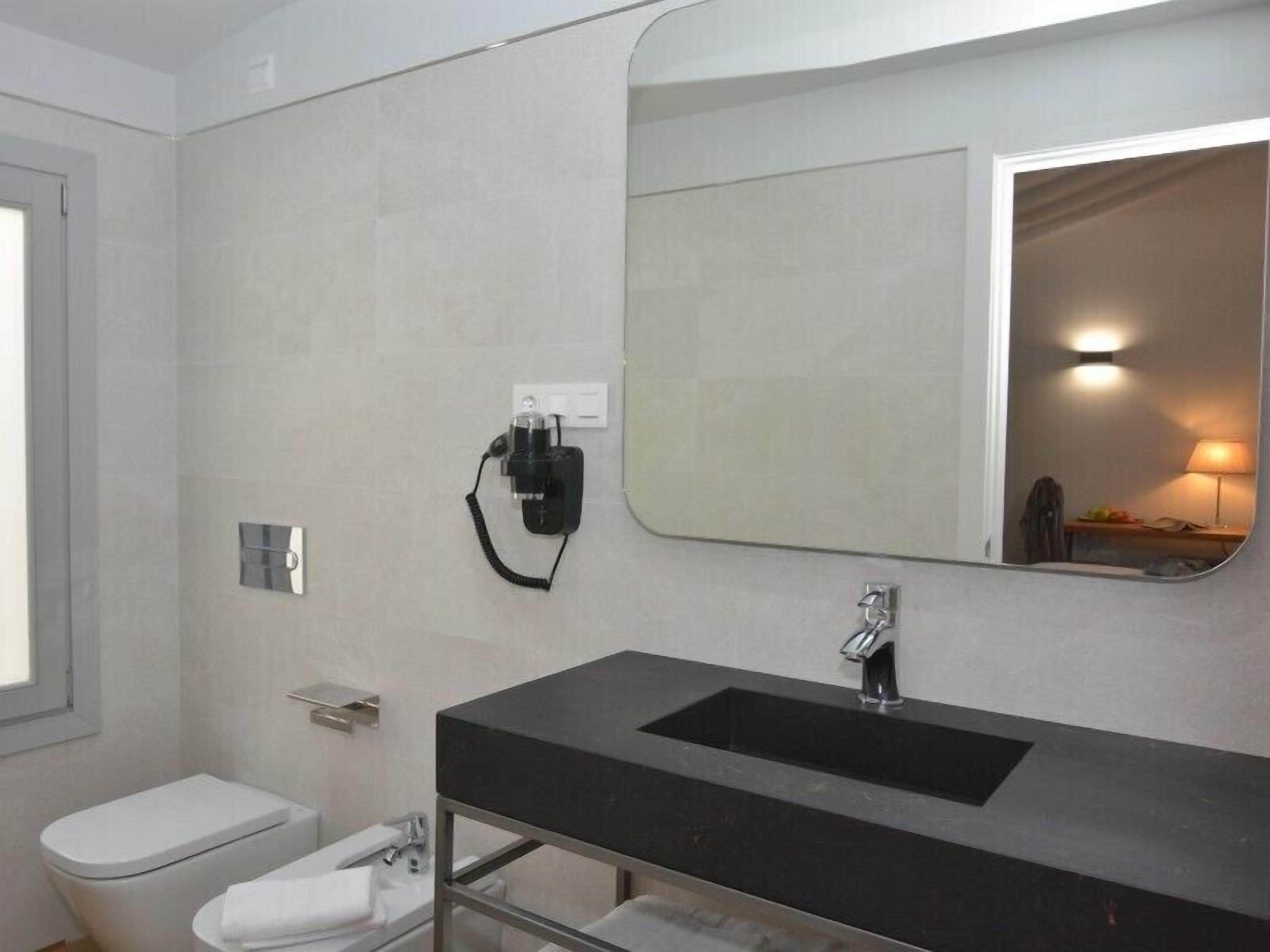 Un baño moderno con un lavamanos negro, un inodoro y un espejo.