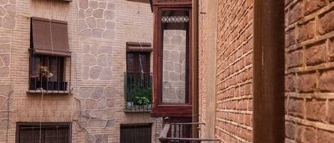 A narrow alleyway with a building featuring stone walls, a wooden door, and a metal railing.
