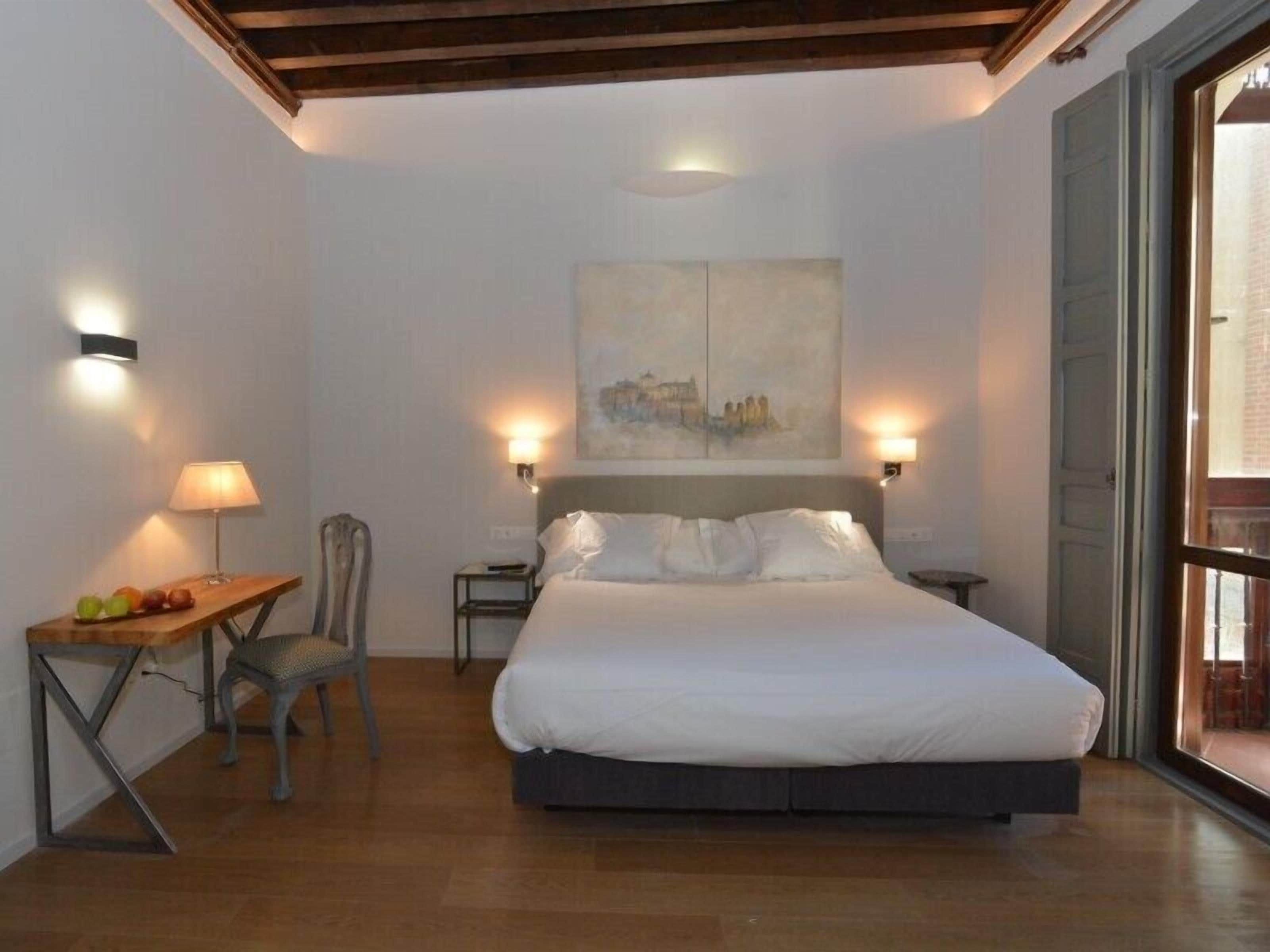 Un dormitorio con una cama, una silla, una mesa con frutas y un cuadro en la pared.