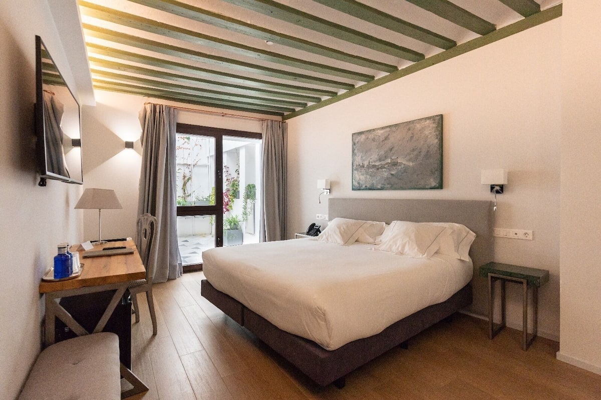 Une chambre d’hôtel avec un lit, un bureau, une chaise, une lampe, un tableau et une vue sur l’extérieur.
