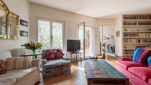 Ein Wohnzimmer mit Sofa, Sessel, Couchtisch, Fernseher, Bücherregal und einem großen Spiegel.