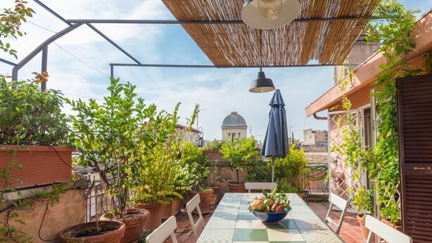 Eine Terrasse mit einem karierten Tisch, Blumentöpfen und Blick auf ein Kuppelgebäude.