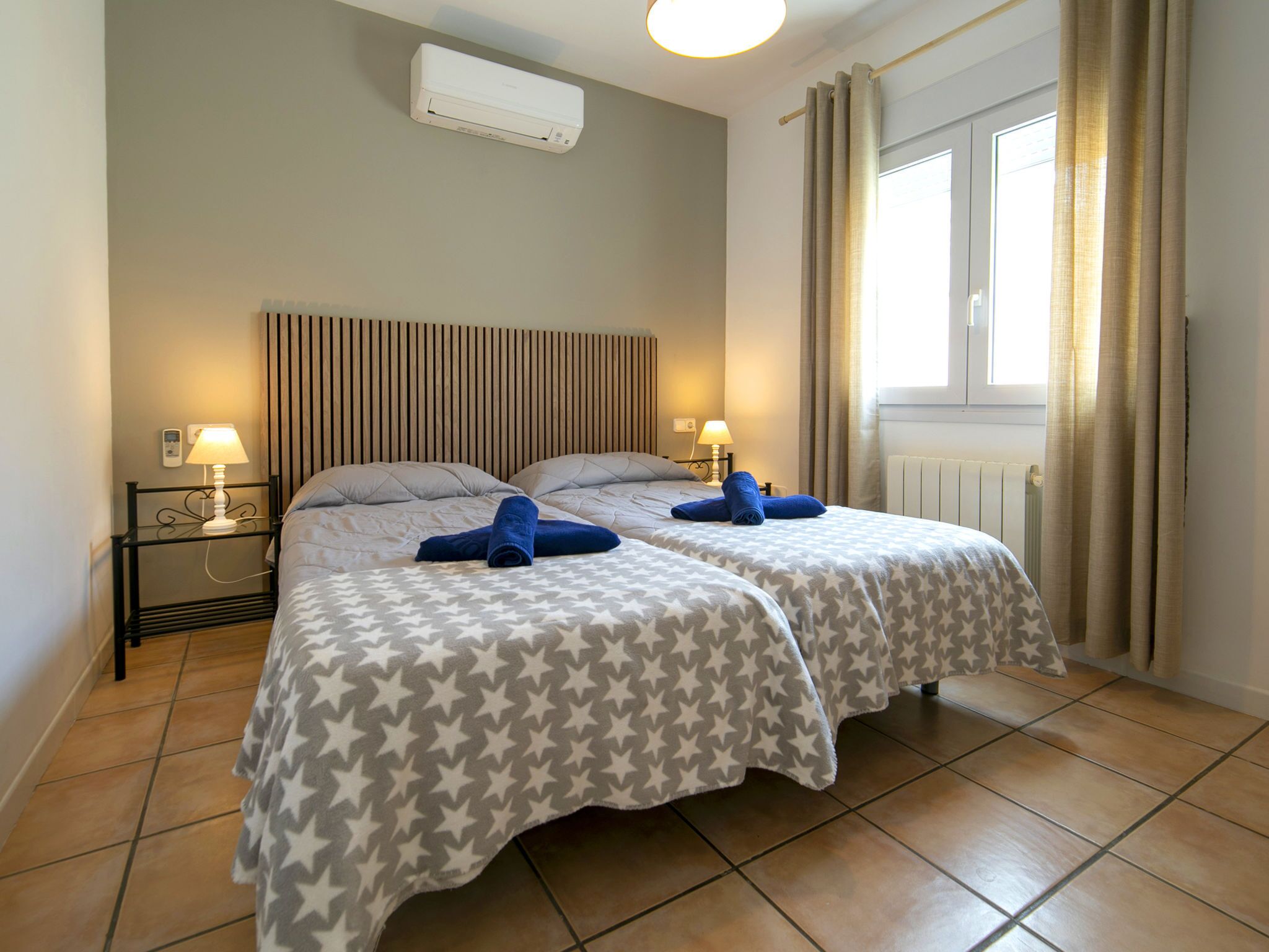 Ein Hotelzimmer mit zwei Betten, einem Fenster mit Vorhängen, einer Klimaanlage und Nachttischlampen.