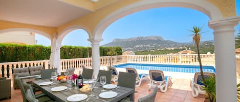 A covered outdoor dining area with a pool and mountain view.