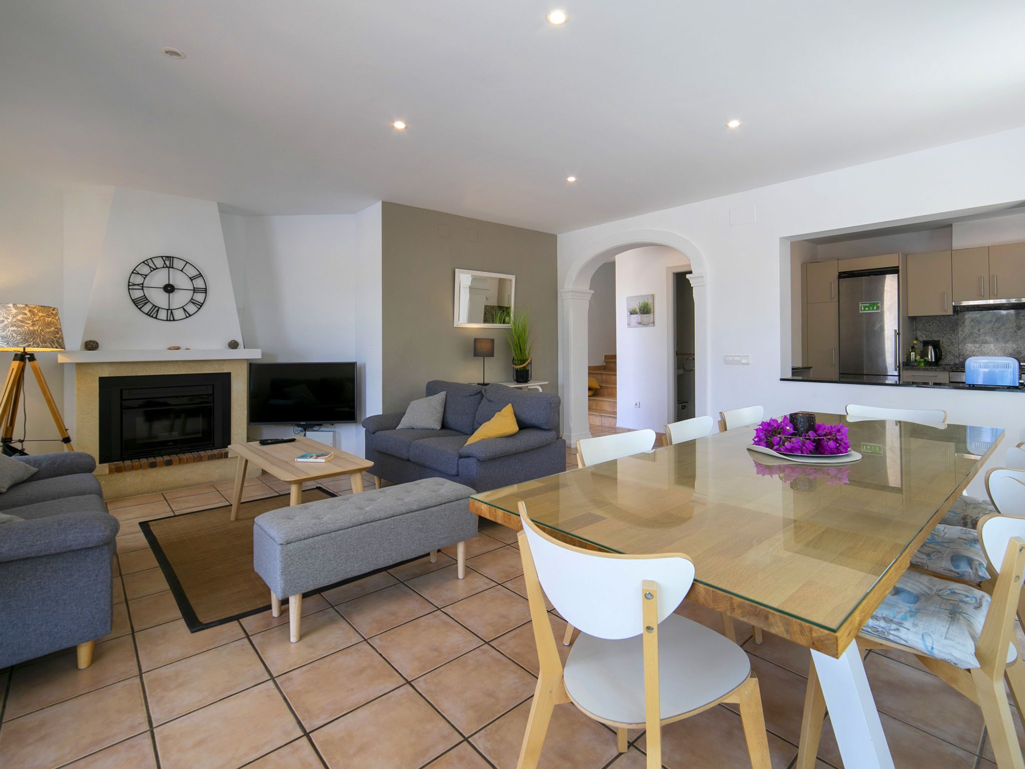 Un salon moderne avec une cheminée, un canapé, un téléviseur et un coin repas comprenant des chaises et une table en verre.