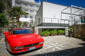A red sports car parked in front of a modern building with a stone facade and potted plants. - My Exclusive Italy - Beachfront Villa Sorrento & private sea access (Sorrento)