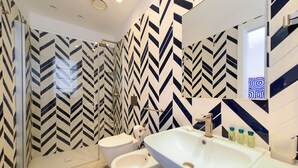 Ein modernes Badezimmer mit einem großen Spiegel, einem weißen Waschbecken und einem Bidet. Die Wände sind mit einem schwarz-weißen Zickzackmuster versehen.