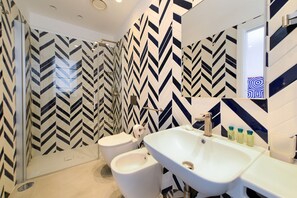 Une salle de bain moderne avec un grand miroir, un lavabo blanc et un bidet. Les murs sont recouverts d’un motif à chevrons noir et blanc.