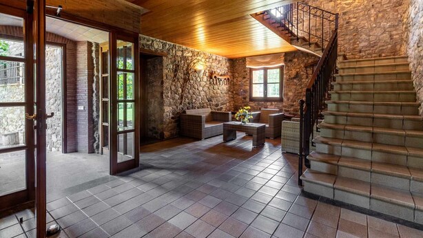 Un intérieur spacieux avec un mur en pierre, un escalier en bois et un coin salon comprenant une table et des chaises.