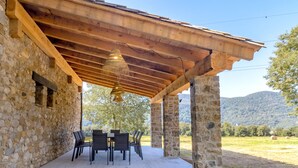 Un espace extérieur abrité, doté de murs en pierre, d’une pergola en bois et d’une table avec des chaises.