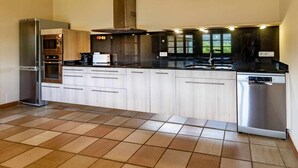 Une cuisine moderne dotée d’appareils électroménagers en acier inoxydable, de meubles de rangement en bois clair et d’un plan de travail noir.
