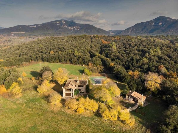 A rural property with two stone buildings, a tennis court, and a surrounding forested area.