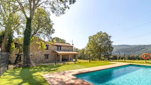 Une maison en pierre avec une piscine, entourée d’une pelouse bien entretenue et d’arbres.