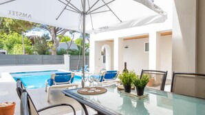 A poolside area with a glass table, blue lounge chairs, and a white umbrella. - New house with private heated pool, parking, wifi, games room (Empuriabrava)