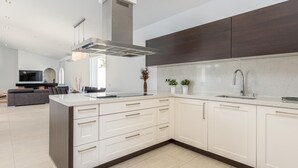 A modern kitchen with white cabinetry, a large island, and a stainless steel range hood. - New house with private heated pool, parking, wifi, games room (Empuriabrava)