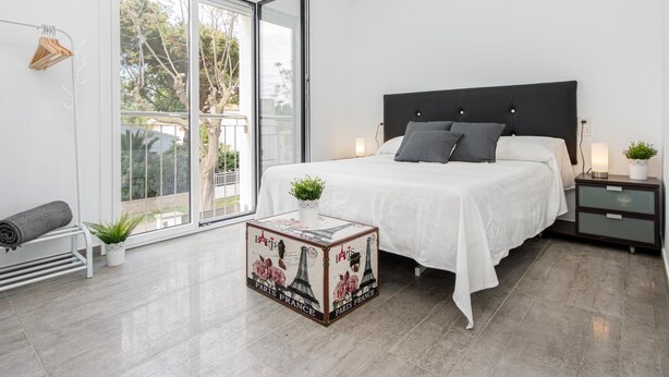 A modern bedroom with a large bed, a nightstand, a small table with a decorative box, and a sliding glass door leading to a balcony. - New house with private heated pool, parking, wifi, games room (Empuriabrava)