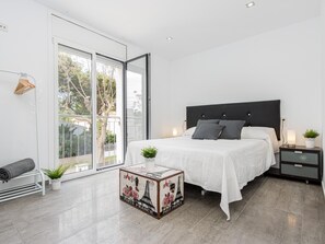 A modern bedroom with a large bed, a nightstand, a small table with a decorative box, and a sliding glass door leading to a balcony. - New house with private heated pool, parking, wifi, games room (Empuriabrava)