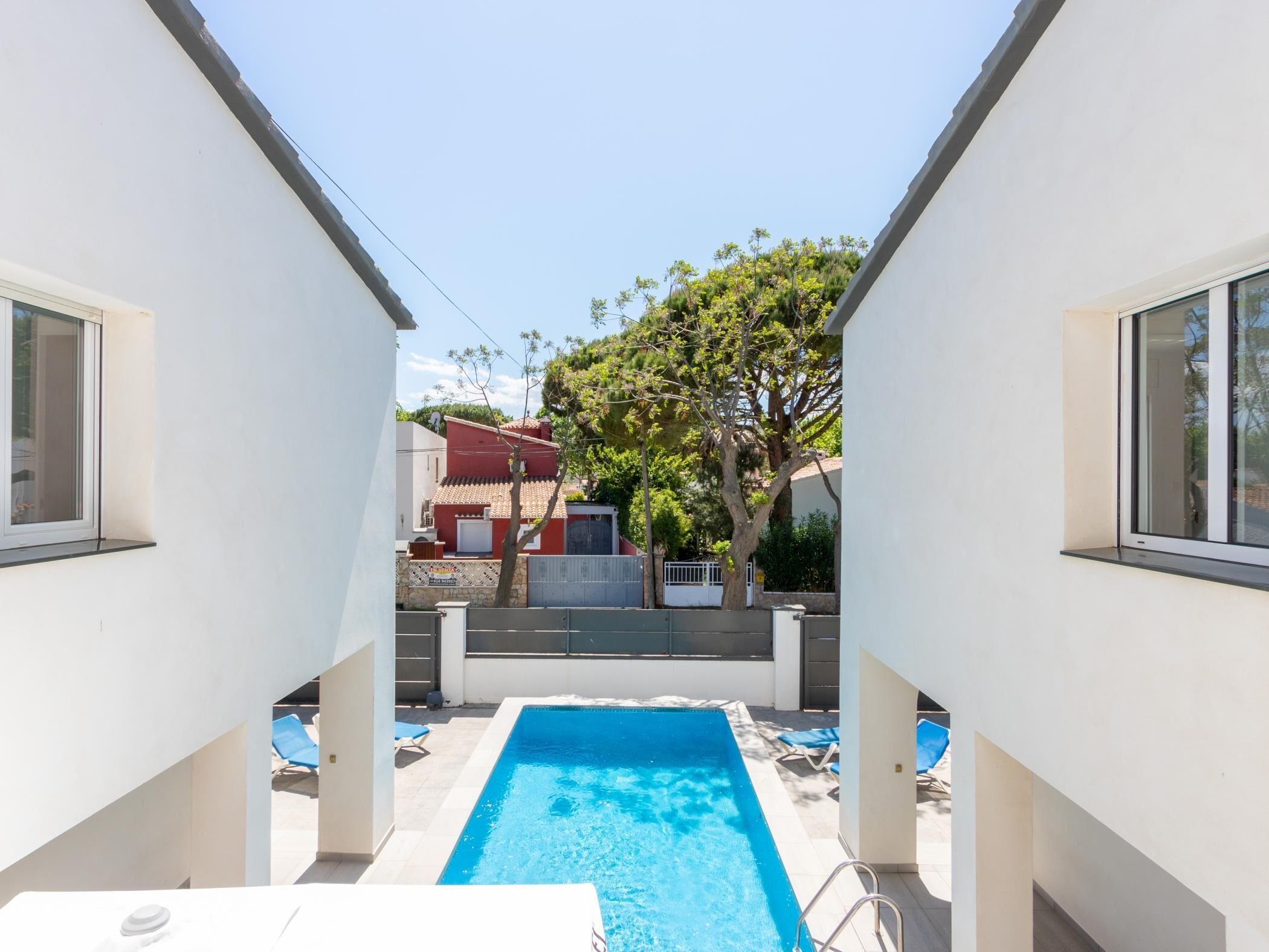 A swimming pool with a clear blue water, surrounded by white walls and a tree.