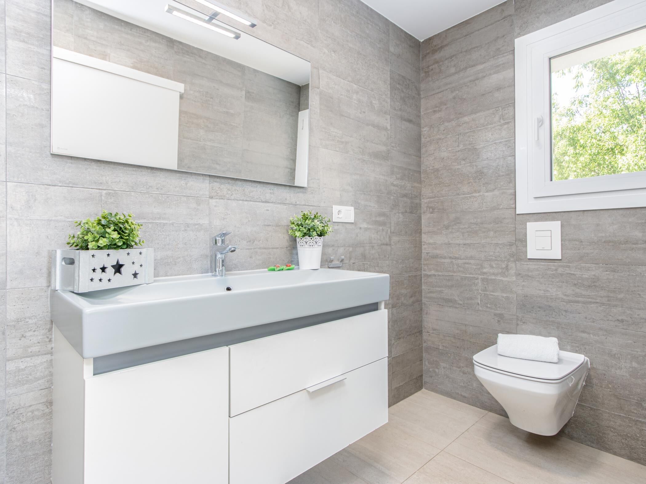 A modern bathroom with a large mirror, white vanity, and a toilet.