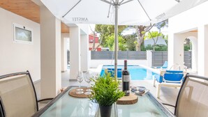 A glass-top table with a potted plant, two wine glasses, and a bottle of wine, under a white umbrella. - New house with private heated pool, parking, wifi, games room (Empuriabrava)