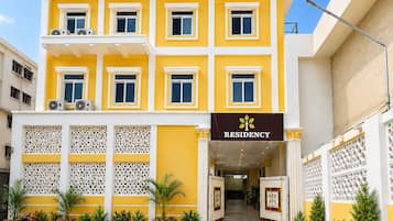 Un edificio de varios pisos con fachada amarilla, una entrada central con un portón decorativo y un letrero que dice 'RESIDENCY'.