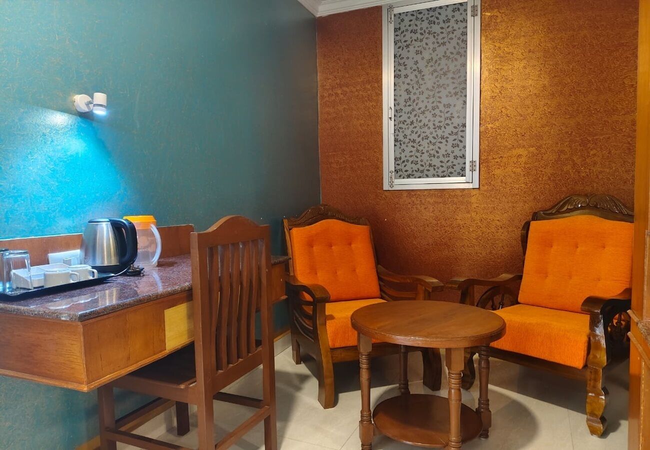 A room with a wooden desk, two orange chairs, a small round table, a window with a floral pattern, and a blue wall.