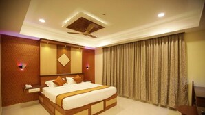 A hotel room with a large bed, a ceiling fan, a nightstand with a phone, and a window with curtains. - I Residency (Puducherry)