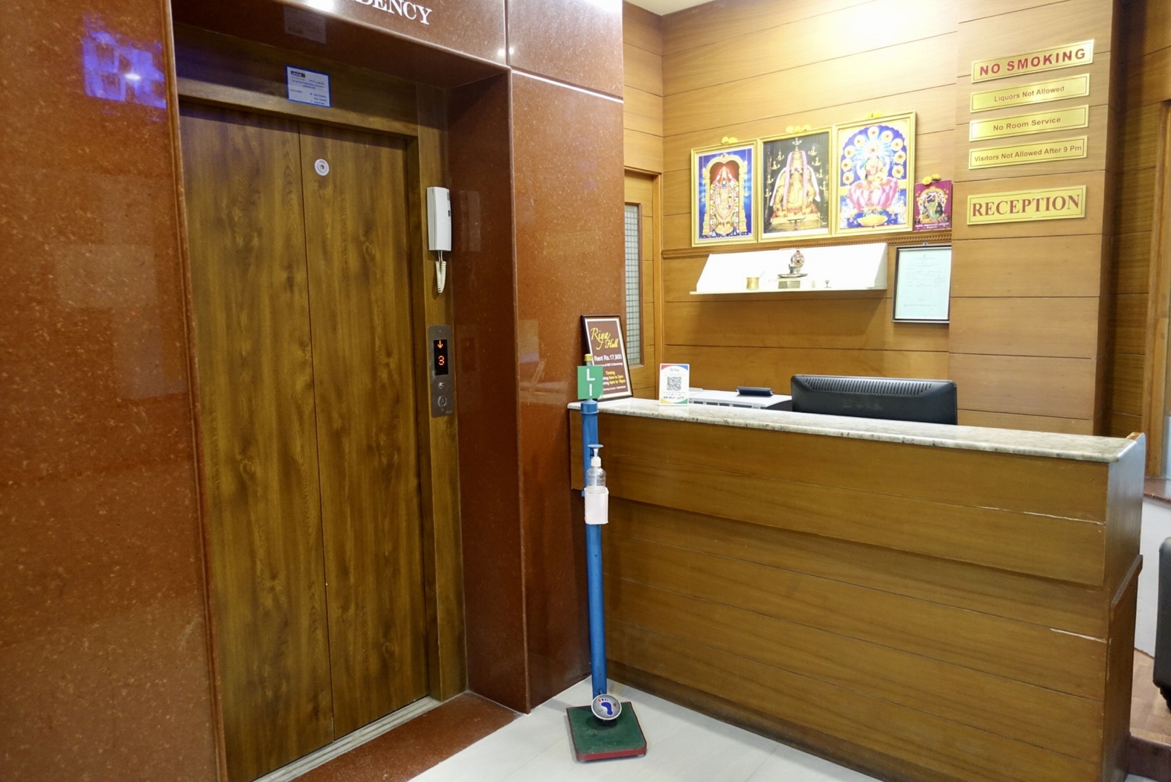 Zona de recepción con mostrador de madera, dispensador de gel antibacterial azul y un letrero en la pared que indica prohibido fumar y recepción.