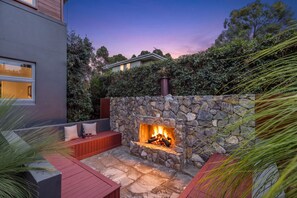 A stone fireplace with a fire, surrounded by a stone wall, and a red bench in a garden setting. - FERNWEH - THE VINTAGE HOLIDAY HOUSES (Rothbury)