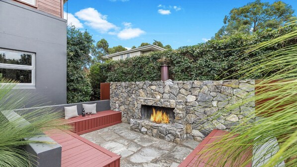 A stone fireplace with a fire, surrounded by a stone wall and a red bench. - FERNWEH - THE VINTAGE HOLIDAY HOUSES (Rothbury)