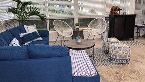 Un salon moderne avec un canapé bleu, deux fauteuils en osier blancs, une table basse ronde et un pouf à motifs.