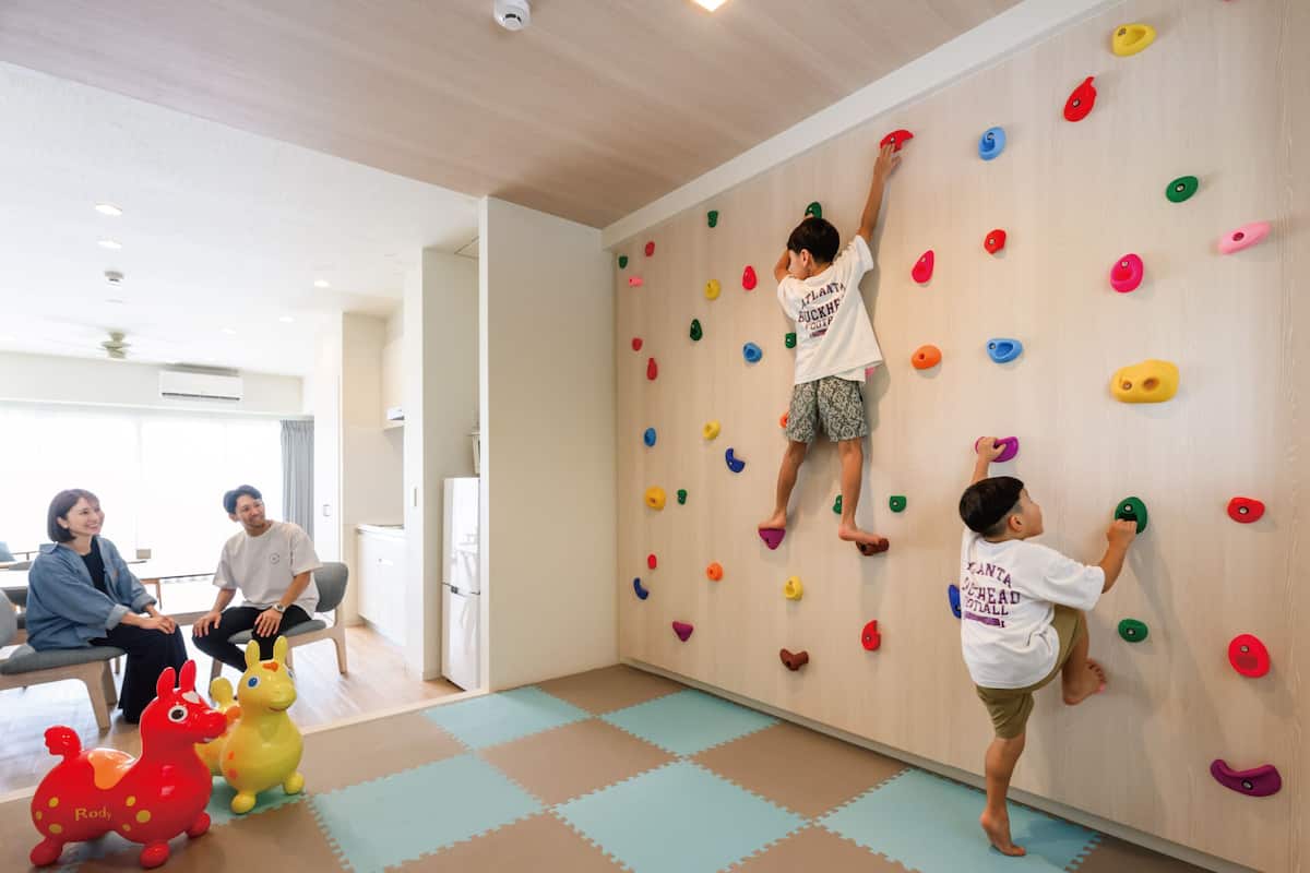 A climbing wall with colorful holds, a play area with foam mats, and a room with a white ceiling and natural light.