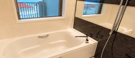 A modern bathroom with a bathtub, a shower, and a large window offering a view of the sea.