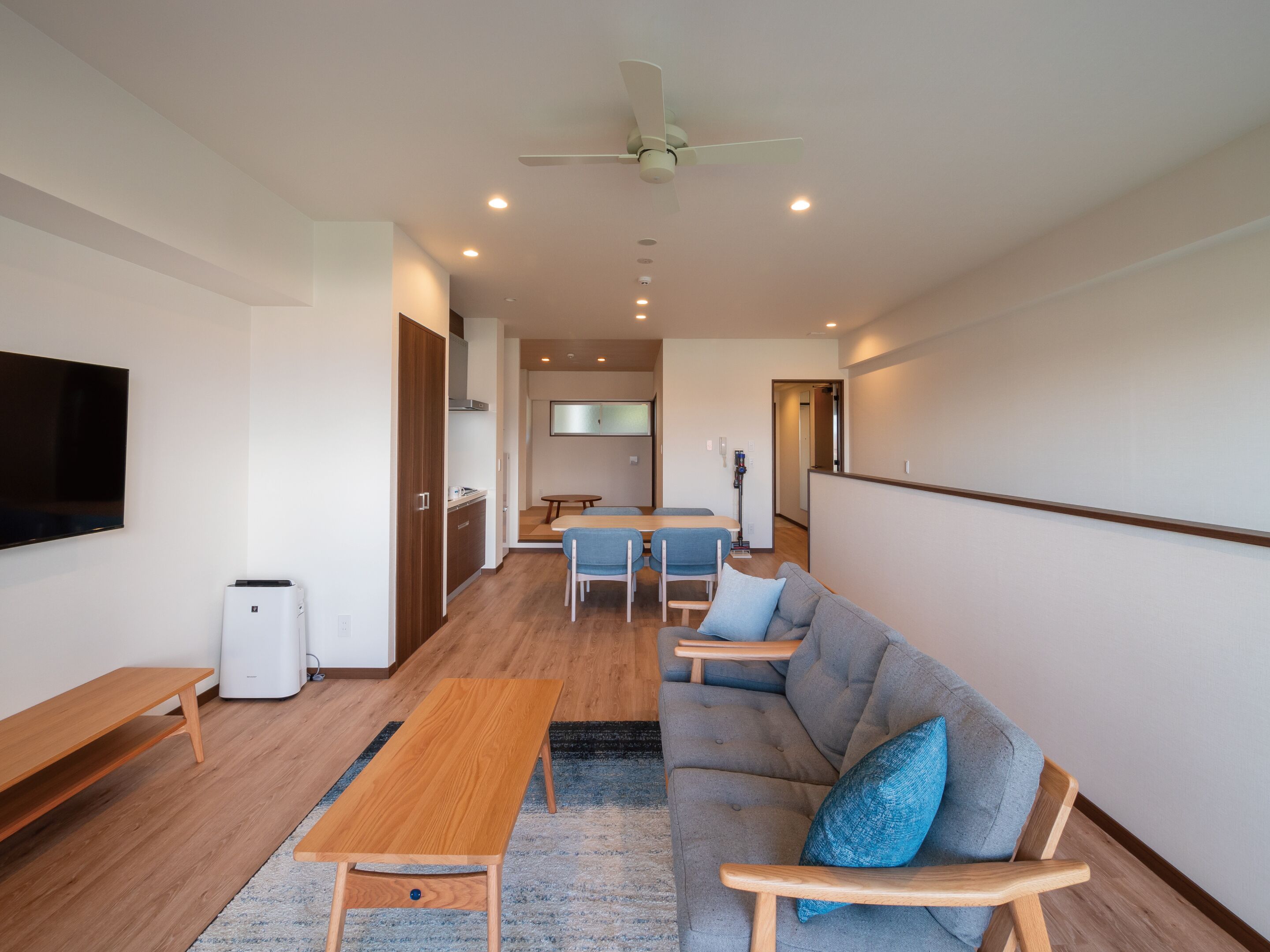 A modern living room with a sofa, a coffee table, a TV, and a kitchen area in the background.