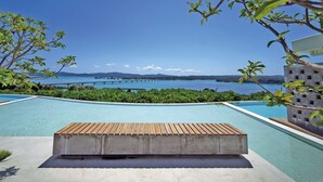 Ein Schwimmbecken mit Holzterrasse im Vordergrund und Blick auf eine Küstenlandschaft mit Bergen und einer Brücke im Hintergrund.