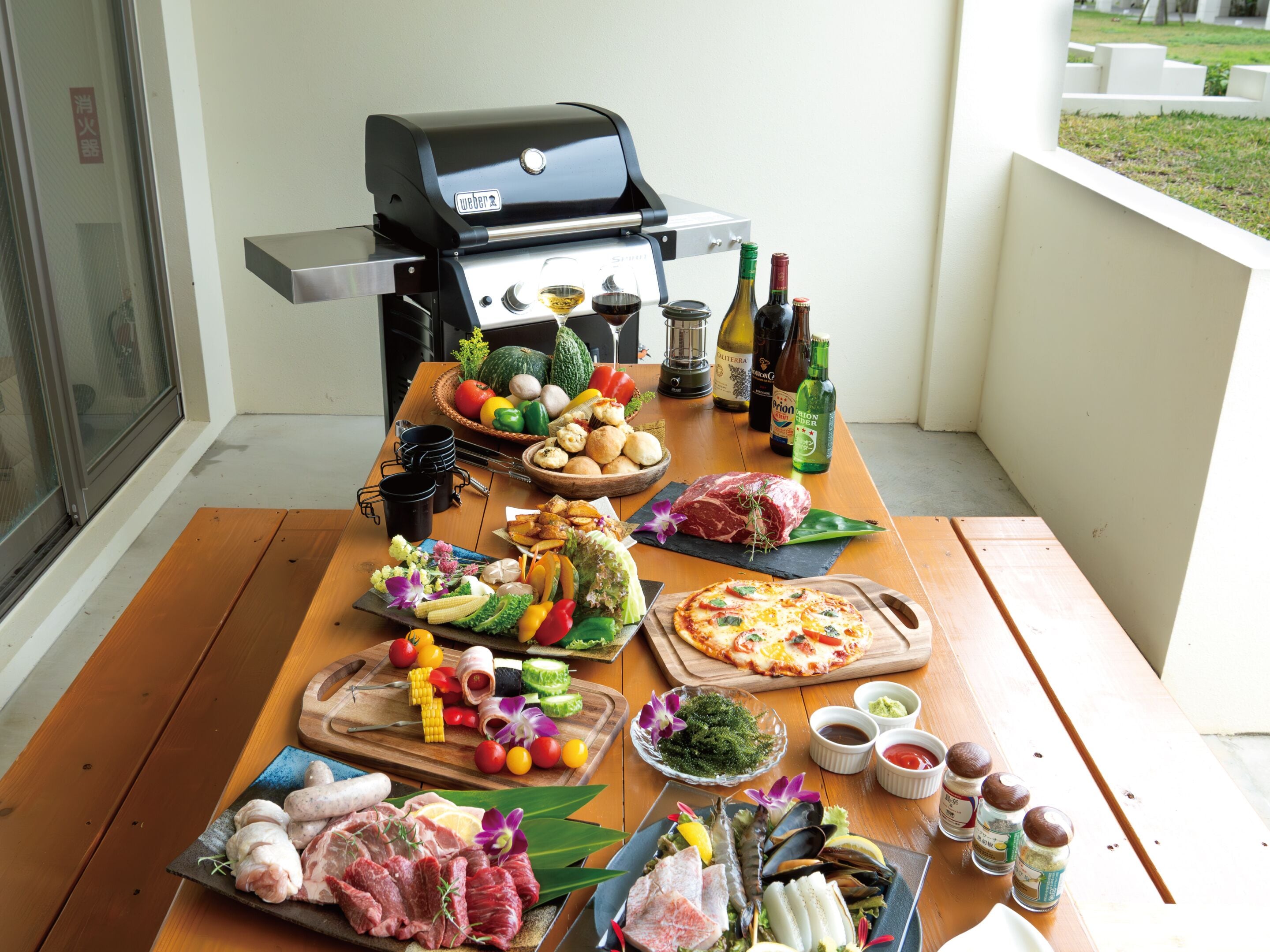 A wooden table with a variety of food items, a grill, and condiments.