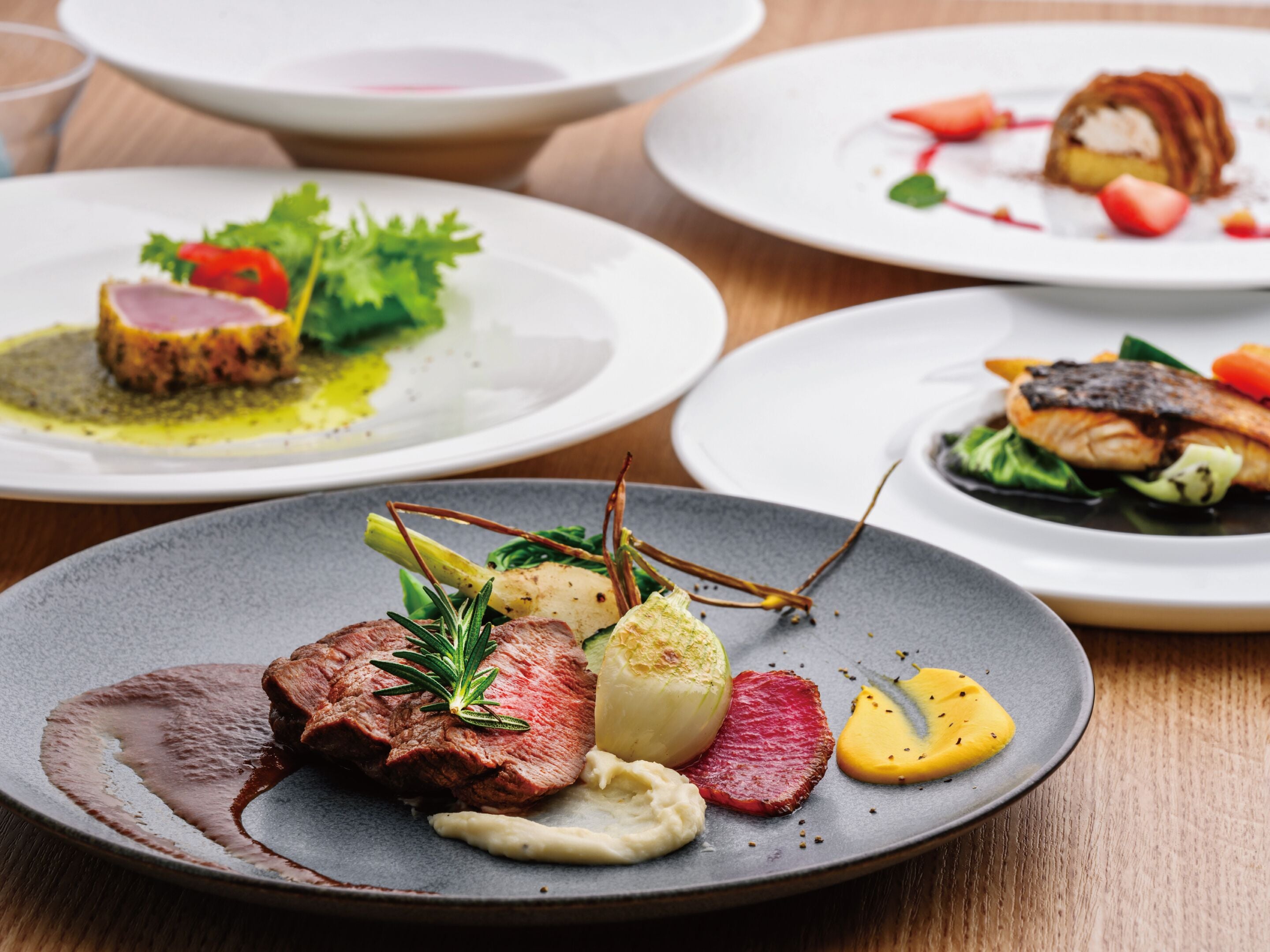 A table with multiple plates of food, including a steak, vegetables, and a fish dish.