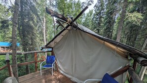 A tent with a wooden deck and two blue chairs.