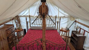 A tented room with a bed, wooden dresser, and a small table with a vase.