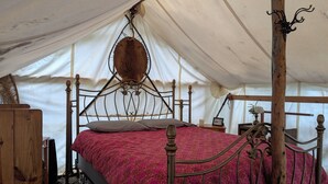 A tent with a bed, wooden furniture, and a hanging light fixture.