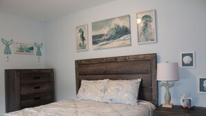 A bedroom with a wooden headboard, a bed with a floral bedspread, and artwork on the walls. - Updated & short walk to downtown Charlevoix! (Charlevoix)