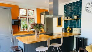 A modern kitchen with a wooden countertop, two bar stools, a stainless steel trash bin, and a built-in oven. - Luxury Apartment-Golden Triangle, Parking & Garden (Norwich)
