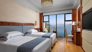 Habitación de hotel con dos camas, televisión, ventana grande con vista al mar y piso de madera.