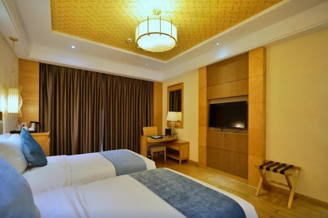 A hotel room with two beds, a desk, a TV, and a wooden bench.
