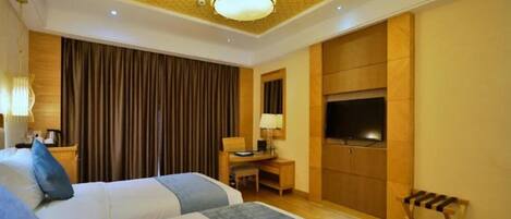 A hotel room with two beds, a desk, a TV, and a wooden bench.