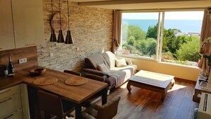 Una sala de estar acogedora con una mesa de comedor de madera, un sofá y un amplio ventanal con vistas al mar.