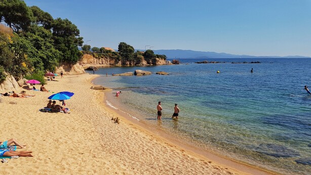 Una playa arenosa con agua cristalina, sombrillas y gente.