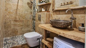 Un baño con lavamanos de piedra, inodoro, ducha y estantes de madera.