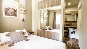 Un dormitorio con una cama grande, un armario de madera, una lavadora y cuadros en la pared.